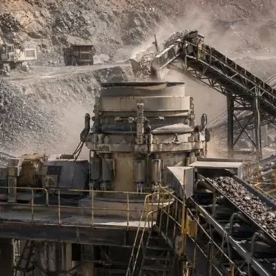 Reduce Crusher Downtime Cone crusher operating at a large mining site with conveyors moving material, supporting efforts to reduce crusher downtime.