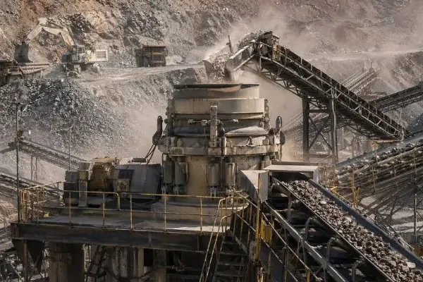 Reduce Crusher Downtime Cone crusher operating at a large mining site with conveyors moving material, supporting efforts to reduce crusher downtime.